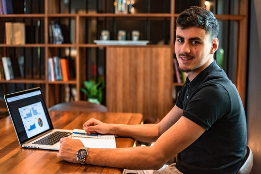 A male college student studying in a university library a young happy man working on laptop with graphs, charts, diagrams on screen in the office workplace.