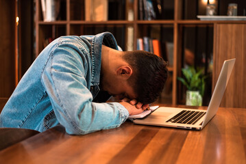 A tired student sleeping on the table while studying or working inside university library or office.