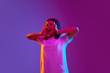 Portrait of excited, happy, smiling young girl standing with positive shocked face on gradient purple background in neon light. Surprise. Concept of emotions, youth, feelings, fashion, lifestyle, ad