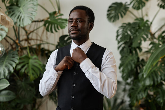 Waist up portrait of handsome black man wearing tux as groom getting ready for wedding, copy space