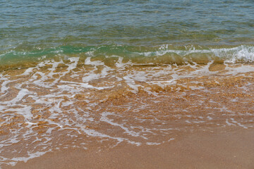 White waves rolls on sandy shore of Black Sea Anapa. White splashes and foam in foreground. Emerald-blue transparent sea water washes yellowish sand. Sea at southern resort of Russia.