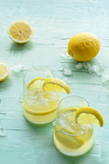 Lemonade. Lemon water drink with ice. Two glasses and fruits on a blue background. Detox beverage. Fresh homemade cocktail