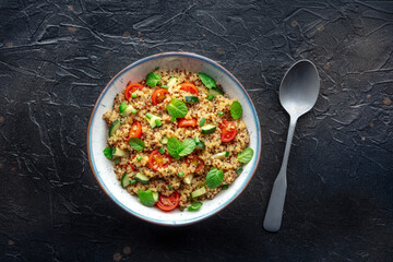 Quinoa tabbouleh salad in a bowl, a healthy dinner with tomatoes and mint, overhead shot with a spoon