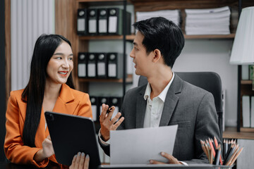Business documents on office table with tablet and laptop computer and chart and two colleagues discussing data in office.