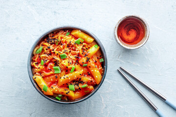 Rabokki, tteokbokki or topokki with ramen, Korean street food, spicy rice cakes in red pepper gochujang sauce, overhead flat lay shot with chopsticks and a drink