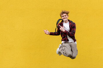 guy student with backpack jumps against the background of yellow isolated wall and shows his hands...
