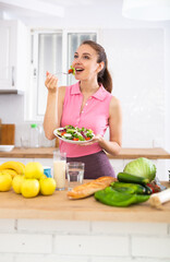 Portrait of woman standing in home kitchen and tasting vegetable salad