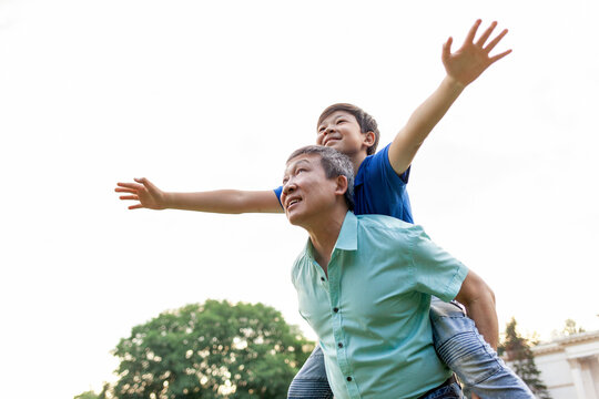 asian boy flying forward on dad's back in summer, korean senior pensioner playing with child in summer outdoors