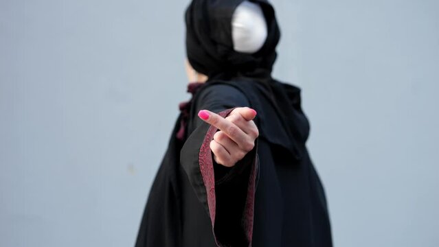 Muslim woman in black hijab disrespects and rejects fellowship and society at grey wall. Lady shows inappropriate gesture being sick of government