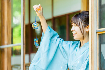 縁側で風鈴を持つ浴衣姿の日本人女性