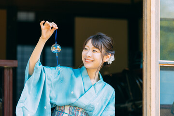 縁側で風鈴を持つ浴衣姿の日本人女性