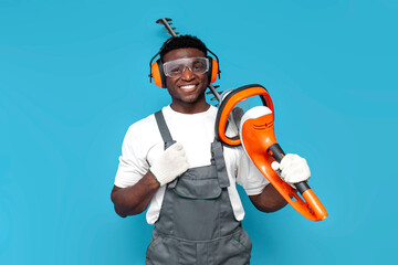 garden worker in uniform holding electric brush cutter on blue isolated background - obrazy, fototapety, plakaty