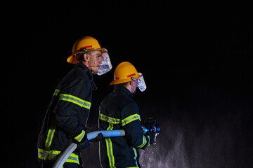 Firefighters using a water hose to eliminate a fire hazard. Team of female and male firemen in dangerous rescue mission. 