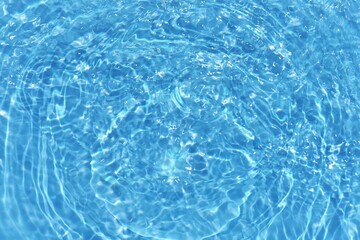Blue water with ripples on the surface. Defocus blurred transparent blue colored clear calm water surface texture with splashes and bubbles. Water waves with shining pattern texture background.