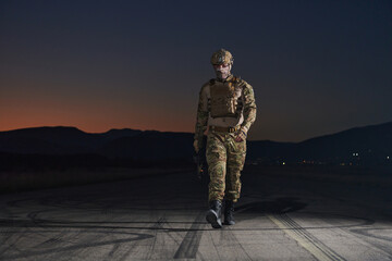 A professional soldier in full military gear striding through the dark night as he embarks on a perilous military mission