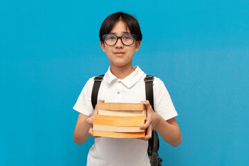 asian boy schoolboy of twelve years old wearing glasses and with backpack holds lot of books