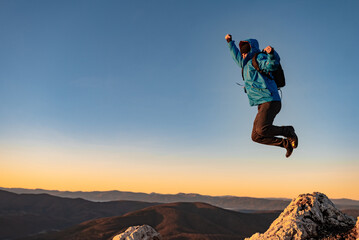 A happy joyful man jumping on top of a mountain concept of adventure travel extreme sport hiking.