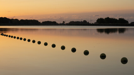 A line of buoys reclected in a calm lake during sunrise