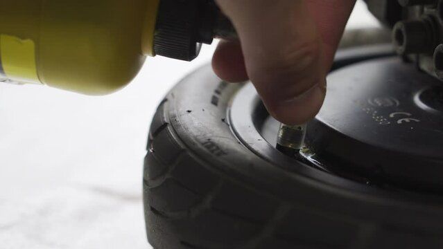 Repairing a punctured wheel with sealant. A man fills a damaged electric vehicle tire with sealant. Close-up