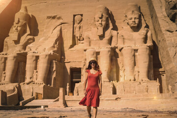 A young tourist in a red dress leaving the Abu Simbel Temple in southern Egypt in Nubia next to...
