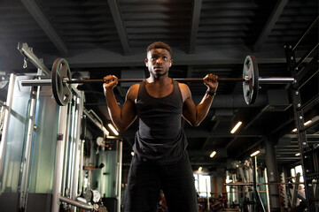 african american man lifts barbell in dark gym, sports guy trains in fitness room and goes in for...