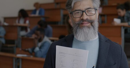 Slow motion portrait of cheerful professor holding paper for English test while students writing passing examination. People and education concept.