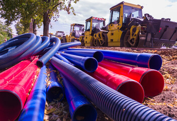 Column of yellow bulldozers and stacked water and sewer pipes on new road construction site