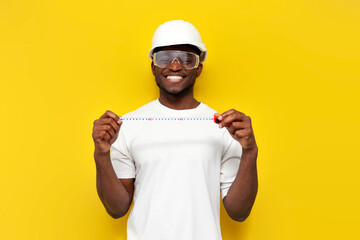 male african american builder in uniform holds tape measure on yellow isolated background