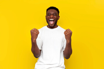 african american man in white t-shirt celebrates victory and raises his hands up on yellow isolated background - Powered by Adobe
