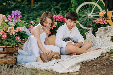 Naklejka premium Kids on picnic with rabbits or bunny at sumer or spring with blooming garden park. Happines on nature children