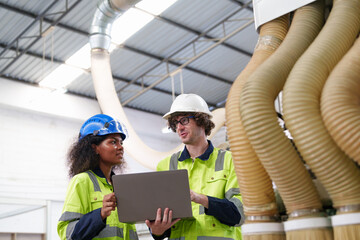 Diverse engineering team analyzing system operations near industrial ducts in factory, highlighting...