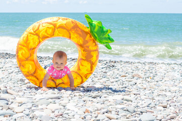 Cute funny little toddler girl on the beach near to the sea with a swimming ring. Child have fun during summer vacation in tropical resort.