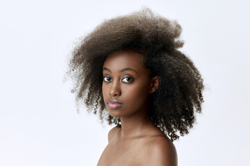 Portrait of beautiful, young, african woman with curly brunette ai and well-keep skin looking at camera against white studio background