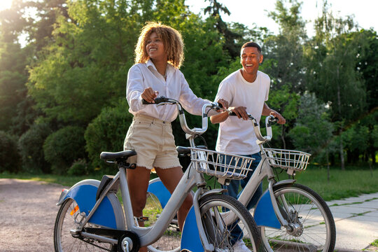 african american couple walking in the park with bicycles and talking, man and woman together with eco transport