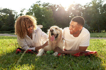 Obraz premium african american guy with girl lie together with golden retriever in the park in summer