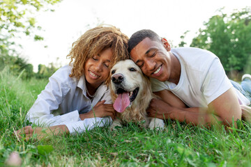 african american happy couple lie together with dog in park in summer, man and woman hug and love...