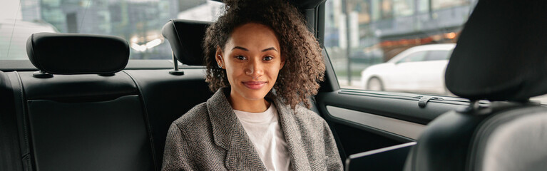 Smiling businesswoman manager working on laptop sitting car leather backseat on the way to office