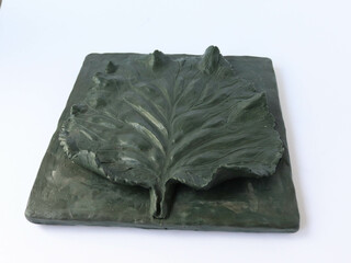 Plasticine sculpture made of a tree leaf. Sculptural artwork in the shape of a linden leaf. Dark green plasticine. Fine, precise details on a white background