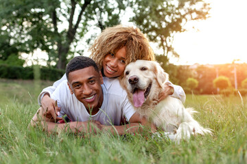 african american guy with girl lie together with golden retriever in the park in summer