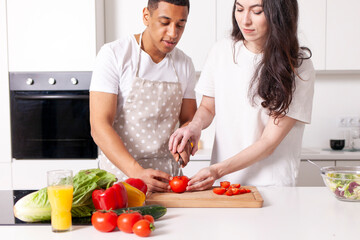 young happy multiracial couple preparing veggie vegetable and greens salad in white kitchen
