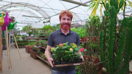 Portrait of a male caucasian redhead customer holding basket of plants and flowers inside horticultural greenhouse plant store