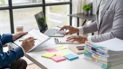 Businessmen use a calculator to calculate company financial statements for their colleagues, view and jointly solve problems within the company. Business finance and accounting concepts