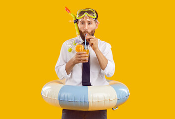 Funny office worker enjoying summer holiday. Portrait of man in office shirt, tie snorkeling mask and beach ring standing isolated in yellow background, holding glass and drinking tropical cocktail © Studio Romantic