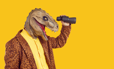 Side profile view studio portrait of happy funny curious excited man in dinosaur mask and leopard costume jacket standing isolated on yellow background, holding binoculars and looking in distance © Studio Romantic