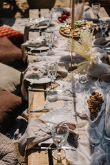 Picnic on beach at sunset in rustic style, boho, food, wine conception. Decor with blanket, pillows, wooden decor, candles, flowers, dry leaves, straw chair. Bachelorette party, birthday, wedding.