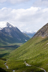 Norwegian mountain Trollstigen, on an early spring day when there is snow on the mountain and the rocks are gray but above them is a blue sky with white clouds and green grass 