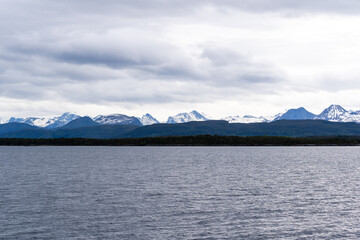 A Norwegian fjord on a harsh overcast day, with dark fjords in the distance and white snow capped with a dramatic sky.