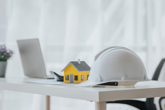 Engineering helmet and small house model, laptop on table construction concept
