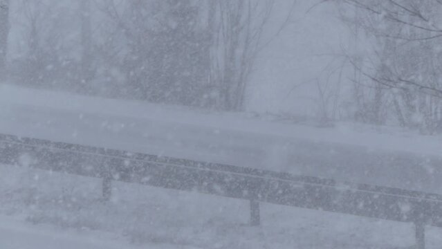 Snowstorm and cars passing on two-way road with poor visibility on road. Winter scene with falling snow on frosty and windy winter day - real time.