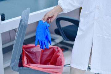 Female doctor throwing infected medical gloves into an infected trash can,Infectious Waste...